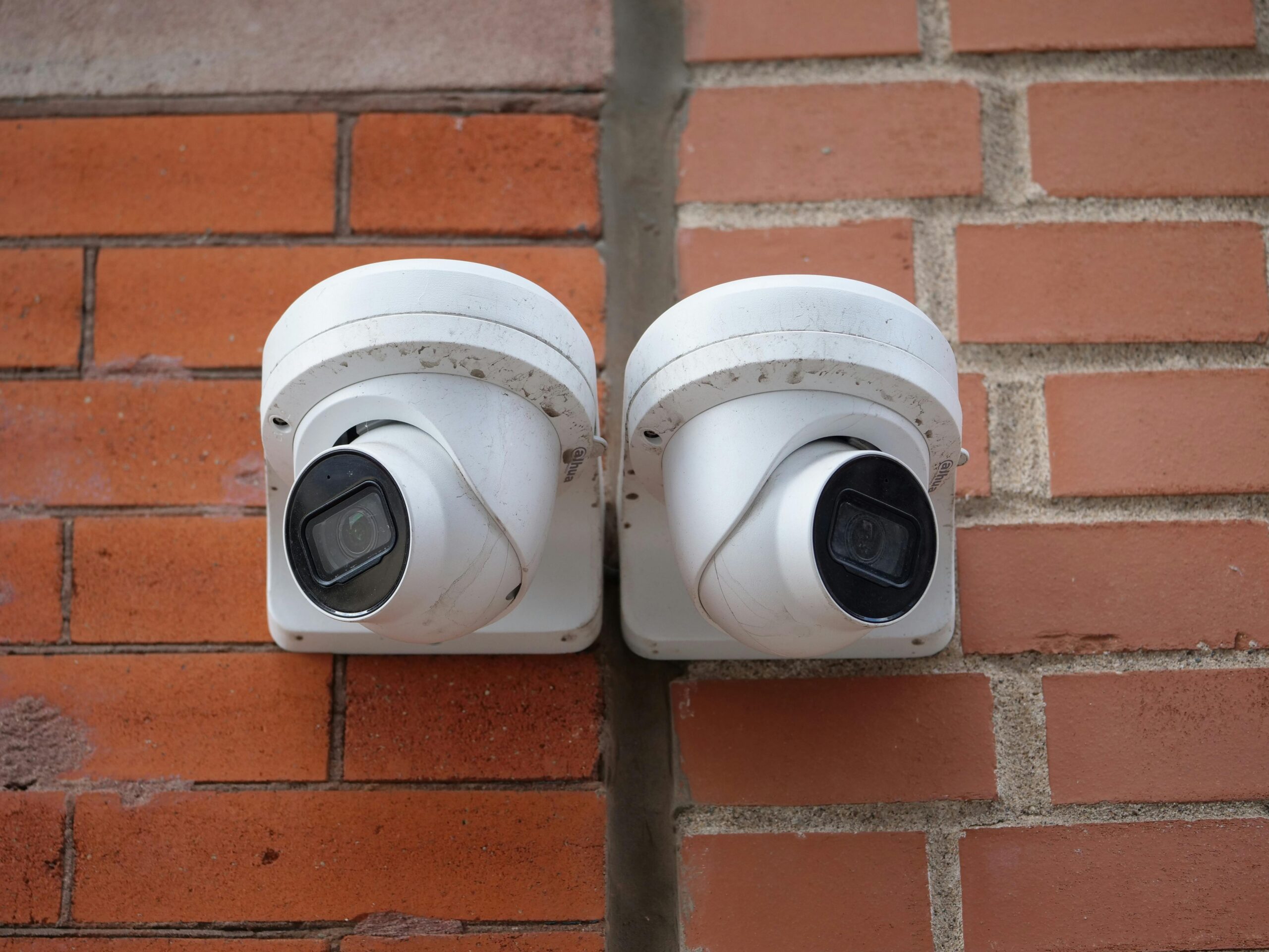 Two white dome security cameras mounted on a brick wall for urban surveillance.